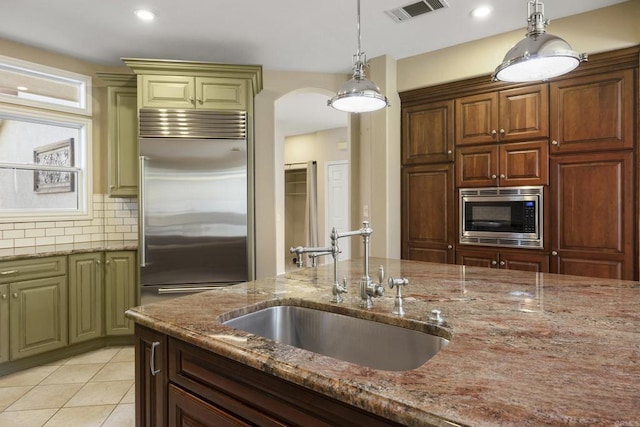 kitchen with built in appliances, light stone counters, hanging light fixtures, decorative backsplash, and sink