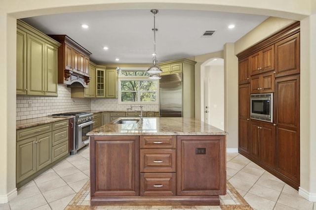 kitchen with a center island with sink, hanging light fixtures, built in appliances, light tile patterned floors, and sink