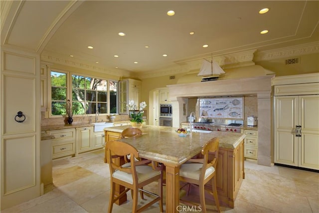 kitchen with cream cabinetry, light stone counters, a kitchen breakfast bar, a kitchen island, and appliances with stainless steel finishes