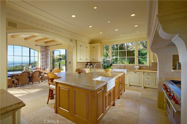 kitchen featuring sink, an island with sink, backsplash, crown molding, and beam ceiling