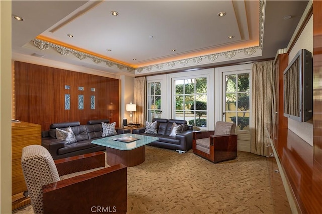 living room featuring a raised ceiling, wood walls, ornamental molding, and carpet flooring