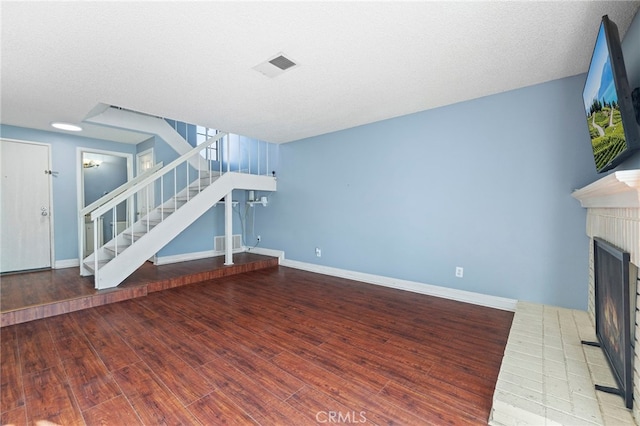 unfurnished living room featuring a brick fireplace, a textured ceiling, and hardwood / wood-style flooring