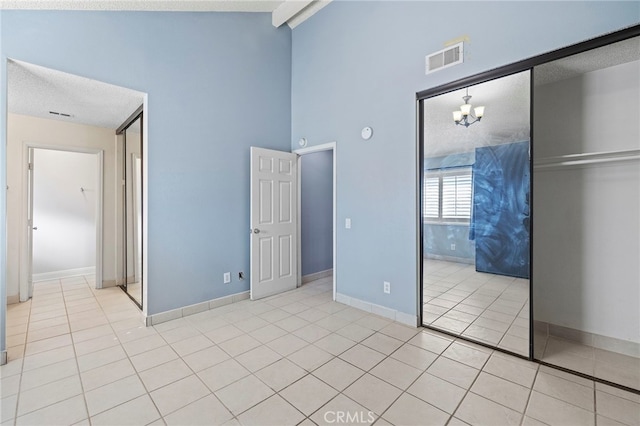 unfurnished bedroom with high vaulted ceiling, a closet, an inviting chandelier, and light tile patterned floors