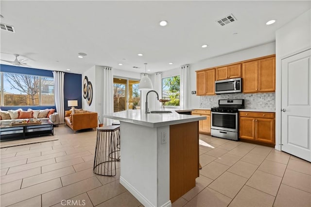 kitchen featuring a kitchen island with sink, backsplash, a breakfast bar area, appliances with stainless steel finishes, and sink