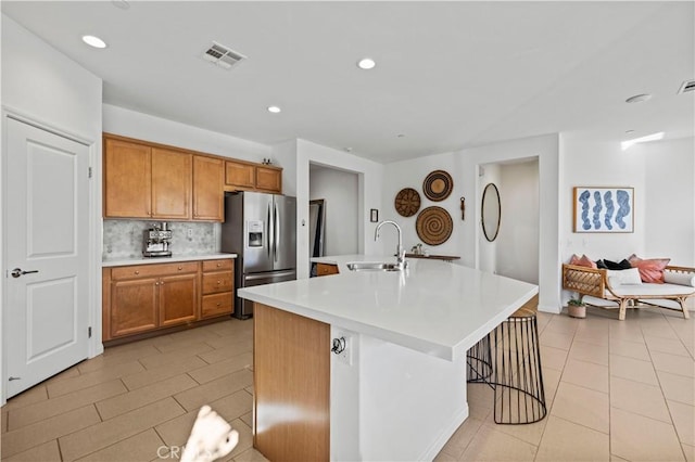 kitchen featuring a center island with sink, a breakfast bar area, stainless steel refrigerator with ice dispenser, sink, and tasteful backsplash