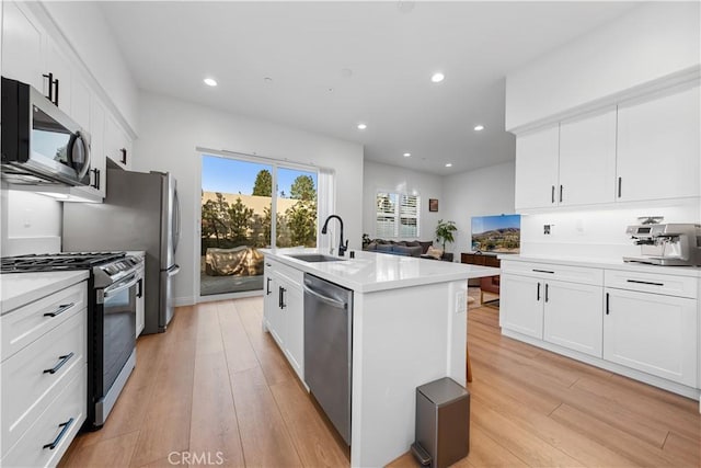 kitchen with white cabinetry, stainless steel appliances, sink, a kitchen island with sink, and light hardwood / wood-style flooring