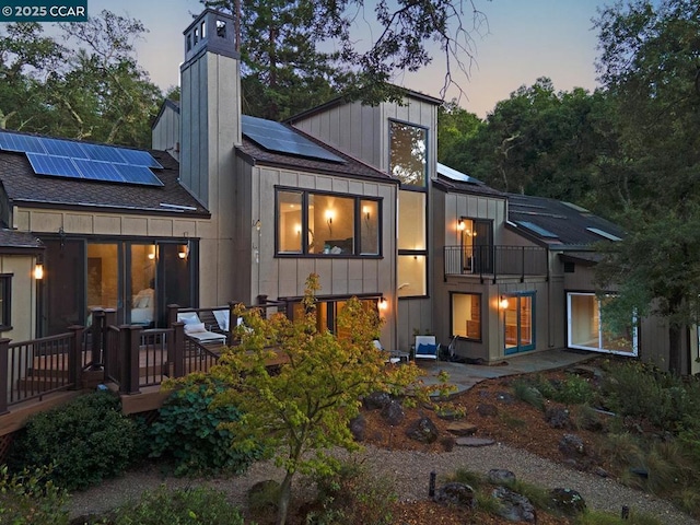 back house at dusk with a deck and solar panels