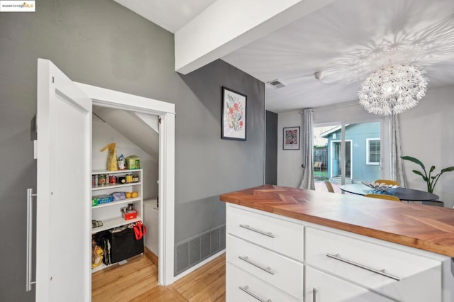 interior space featuring wood counters, a notable chandelier, light wood-type flooring, hanging light fixtures, and white cabinets