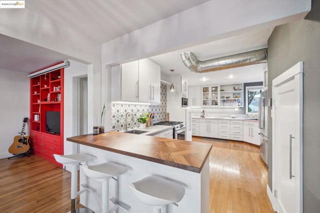 kitchen featuring a kitchen bar, kitchen peninsula, wooden counters, backsplash, and white cabinets