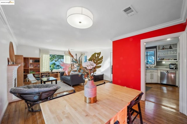 dining room with a fireplace, sink, crown molding, and hardwood / wood-style flooring