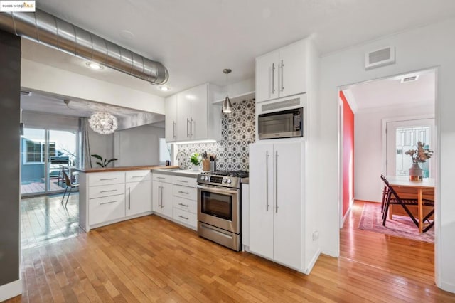 kitchen featuring white cabinetry, kitchen peninsula, appliances with stainless steel finishes, tasteful backsplash, and pendant lighting