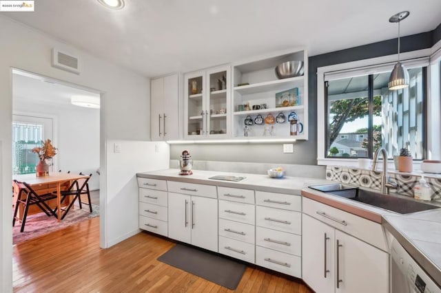 kitchen with dishwasher, decorative light fixtures, white cabinetry, light hardwood / wood-style floors, and sink