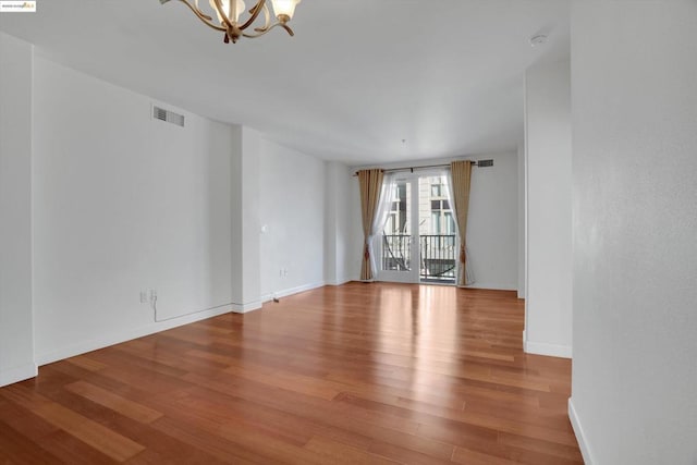 empty room with light wood-type flooring and a notable chandelier