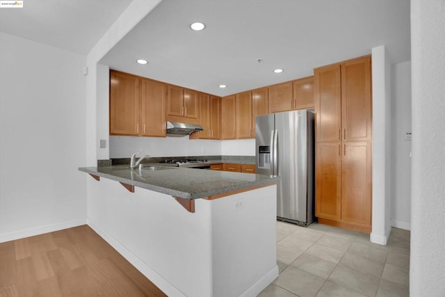 kitchen with sink, stove, kitchen peninsula, stainless steel refrigerator with ice dispenser, and a breakfast bar