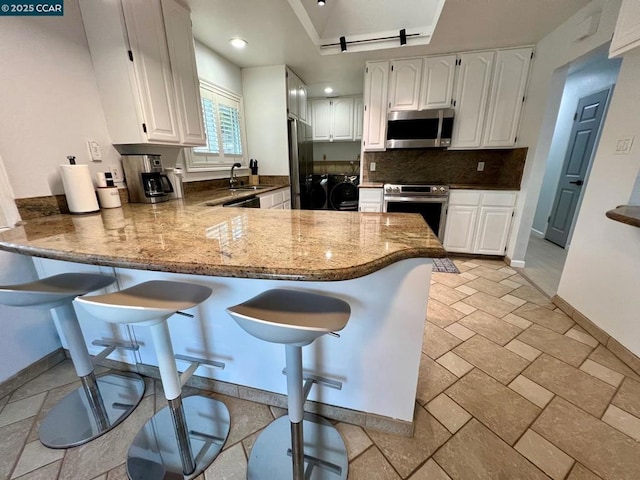 kitchen featuring kitchen peninsula, stainless steel appliances, white cabinetry, stone counters, and separate washer and dryer