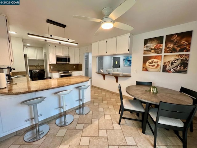 kitchen featuring kitchen peninsula, stainless steel appliances, washer / dryer, stone countertops, and white cabinetry