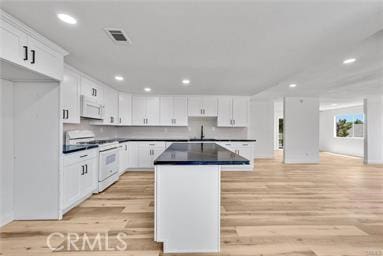 kitchen with white appliances, white cabinetry, a kitchen island, sink, and light hardwood / wood-style flooring