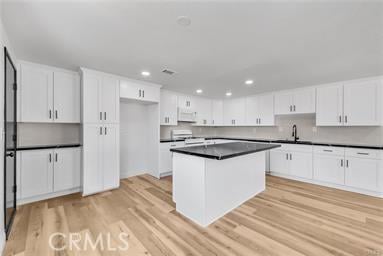 kitchen featuring white cabinetry, a kitchen island, sink, light hardwood / wood-style flooring, and stove