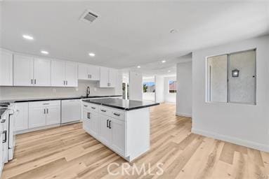 kitchen with white cabinets, a center island, light wood-type flooring, and range