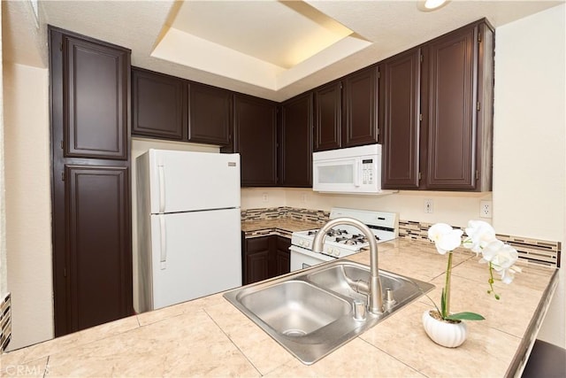 kitchen featuring sink, white appliances, dark brown cabinets, a tray ceiling, and tile counters