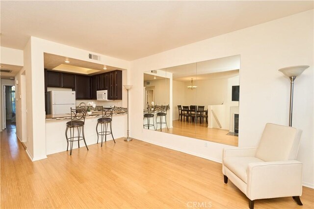 kitchen with white appliances, kitchen peninsula, a kitchen bar, light wood-type flooring, and dark brown cabinets