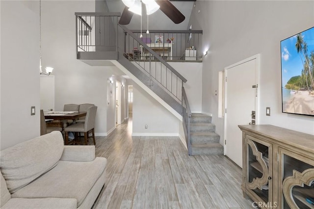 living room with ceiling fan, light hardwood / wood-style floors, and a towering ceiling