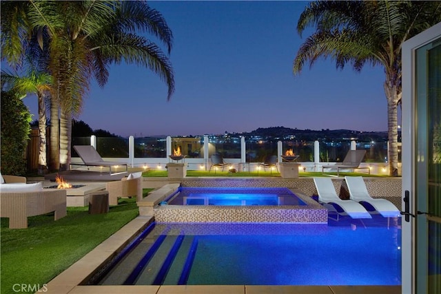 pool at dusk featuring a fire pit and an in ground hot tub