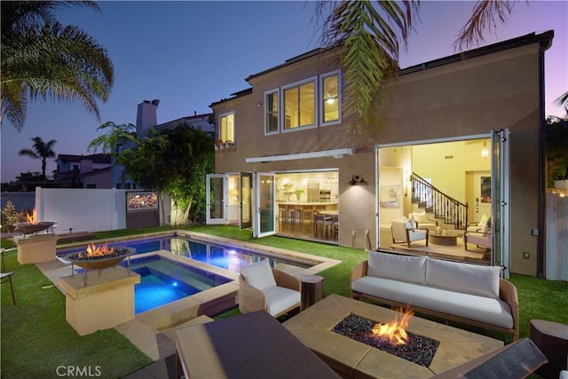 back house at dusk featuring an outdoor living space with a fire pit, a yard, and an in ground hot tub