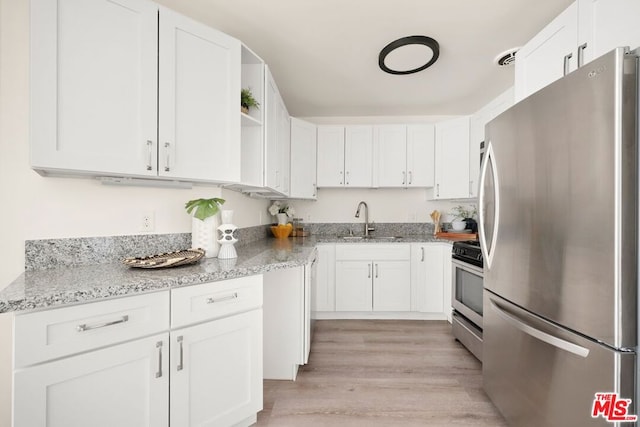 kitchen featuring sink, light stone counters, light wood-type flooring, stainless steel appliances, and white cabinets