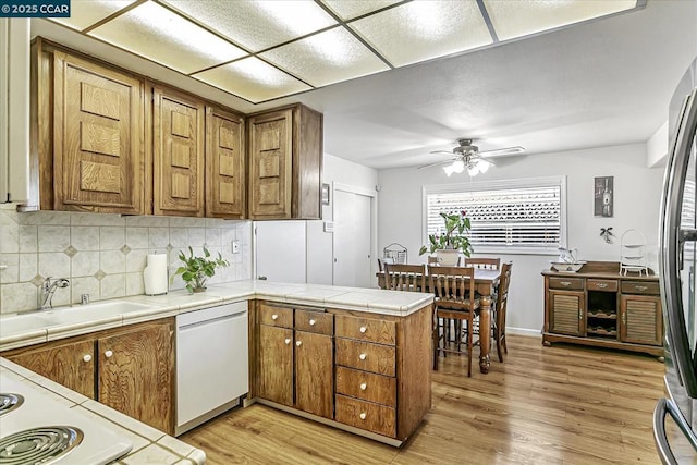 kitchen with tile counters, kitchen peninsula, white dishwasher, sink, and tasteful backsplash