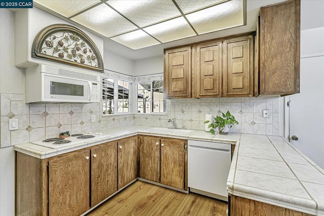 kitchen with sink, white appliances, light wood-type flooring, and tile counters