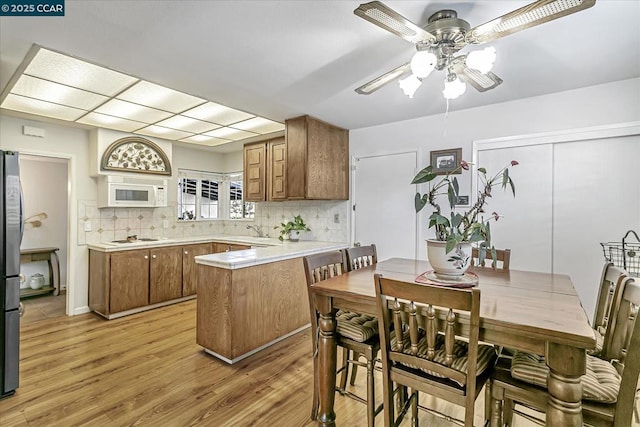 kitchen with white appliances, kitchen peninsula, light hardwood / wood-style flooring, tasteful backsplash, and ceiling fan