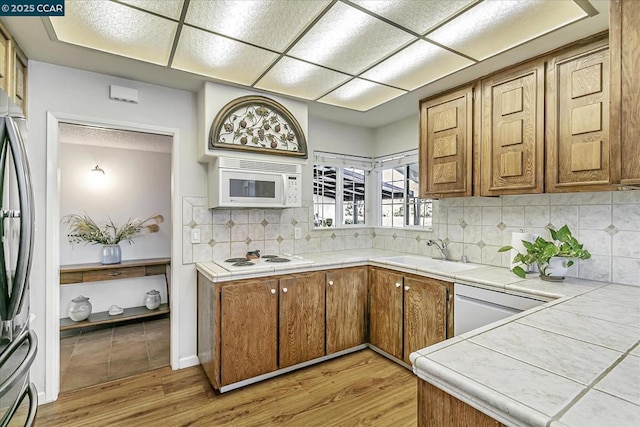 kitchen featuring sink, tile countertops, white appliances, light hardwood / wood-style floors, and decorative backsplash