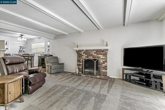 living room featuring a textured ceiling, a brick fireplace, carpet, ceiling fan, and beamed ceiling