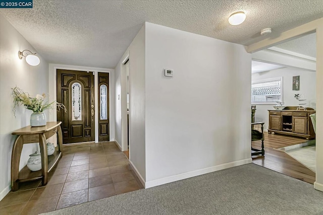 foyer featuring dark tile patterned floors, a textured ceiling, and beamed ceiling