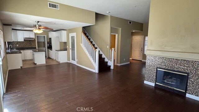 unfurnished living room featuring dark wood-type flooring, ceiling fan, a tile fireplace, and sink