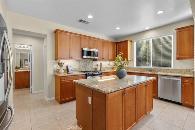 kitchen with stainless steel appliances, light stone counters, a kitchen island, sink, and light tile patterned flooring