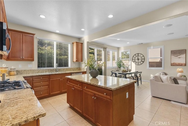 kitchen with sink, light stone counters, light tile patterned floors, a kitchen island, and appliances with stainless steel finishes