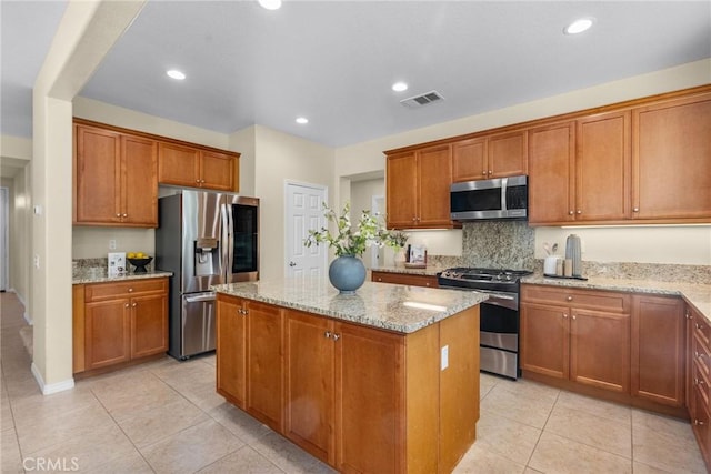 kitchen featuring stainless steel appliances, light tile patterned floors, light stone counters, a kitchen island, and tasteful backsplash