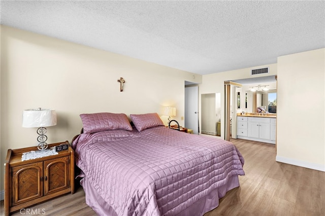 bedroom featuring light hardwood / wood-style floors, a textured ceiling, and ensuite bath