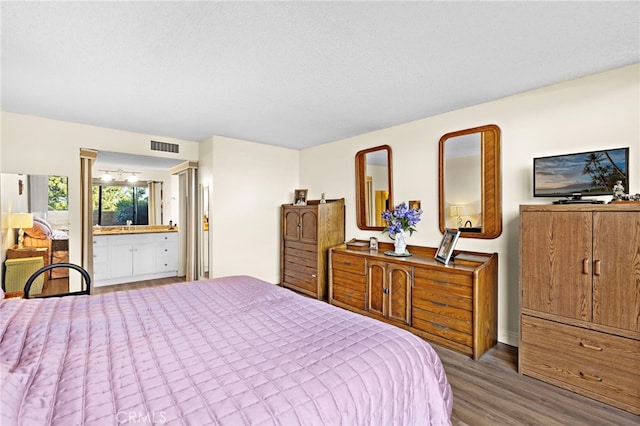 bedroom with connected bathroom, a textured ceiling, and wood-type flooring