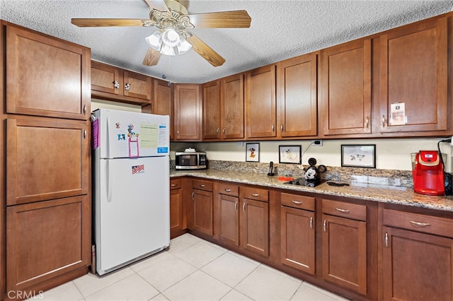 kitchen with ceiling fan, white refrigerator, light tile patterned floors, light stone countertops, and a textured ceiling