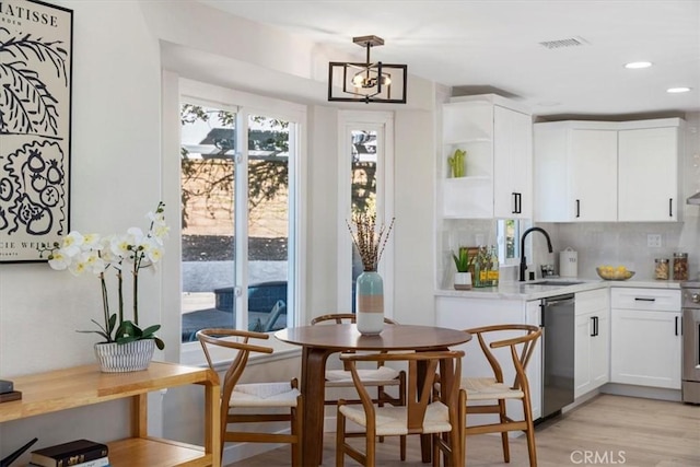 kitchen featuring sink, dishwasher, white cabinetry, hanging light fixtures, and a chandelier