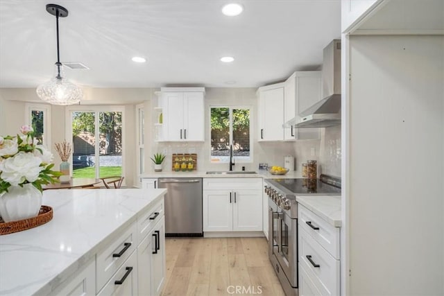 kitchen featuring decorative light fixtures, sink, white cabinets, stainless steel appliances, and wall chimney exhaust hood