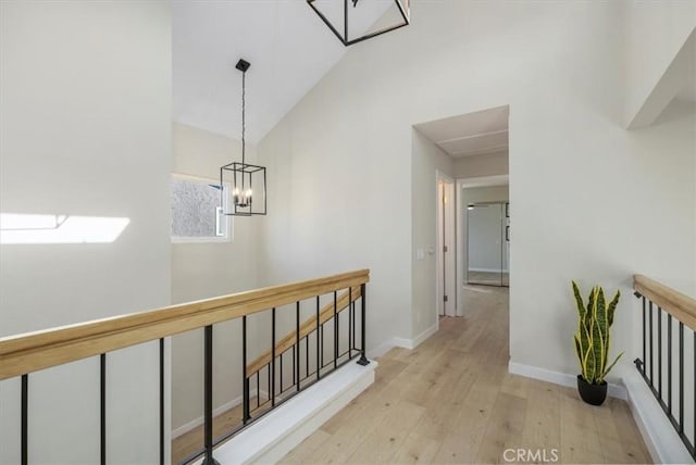 hallway with an inviting chandelier, vaulted ceiling with skylight, and light wood-type flooring