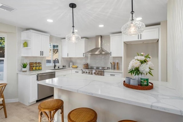 kitchen featuring wall chimney exhaust hood, decorative light fixtures, stainless steel appliances, light stone countertops, and white cabinets