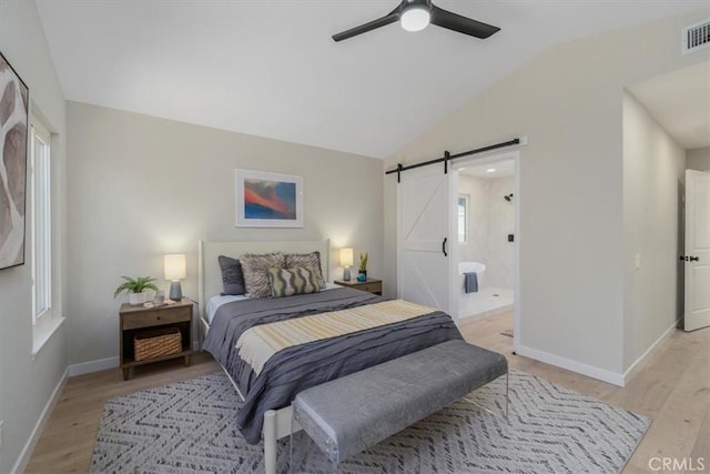 bedroom featuring connected bathroom, vaulted ceiling, ceiling fan, a barn door, and light hardwood / wood-style floors