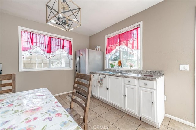 kitchen with sink, white cabinets, light tile patterned flooring, hanging light fixtures, and a chandelier