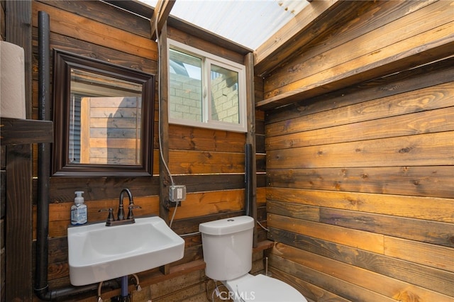 bathroom with sink, wooden walls, and toilet