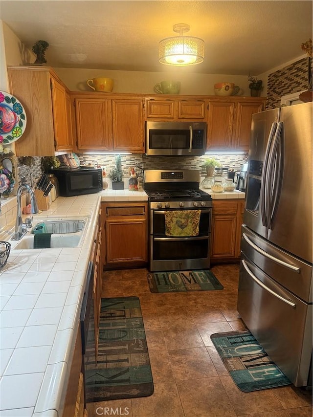 kitchen featuring stainless steel appliances, tile countertops, tasteful backsplash, and sink